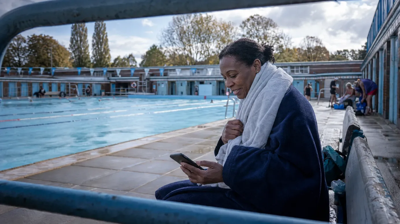 A fundraiser wrapped in a towel replies to a donor beside an outdoor swimming pool.
